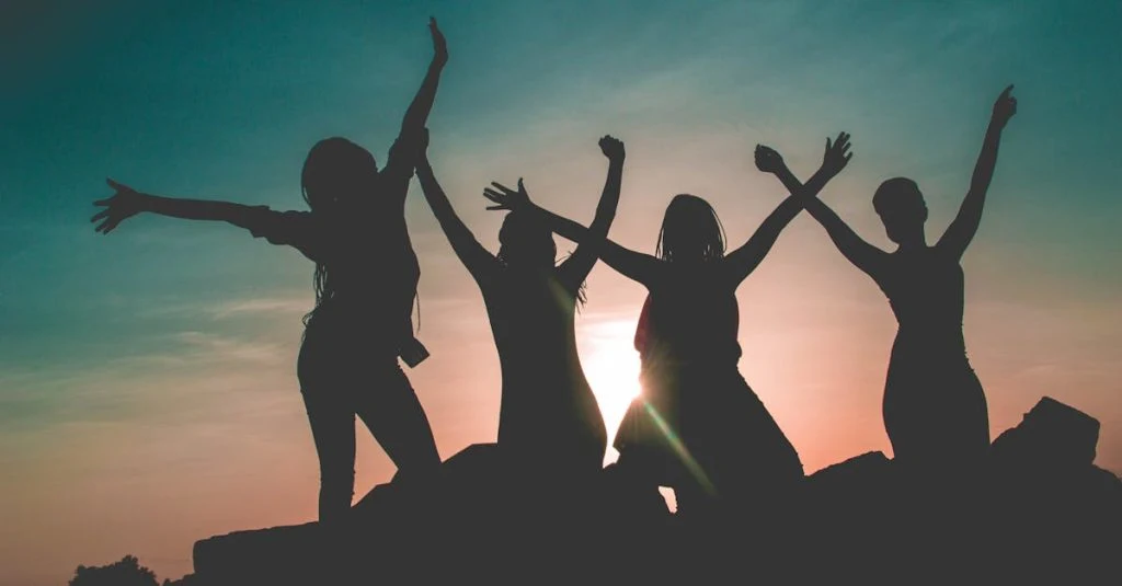 Four women enjoying a fun silhouette moment during a vibrant Kenyan sunset.