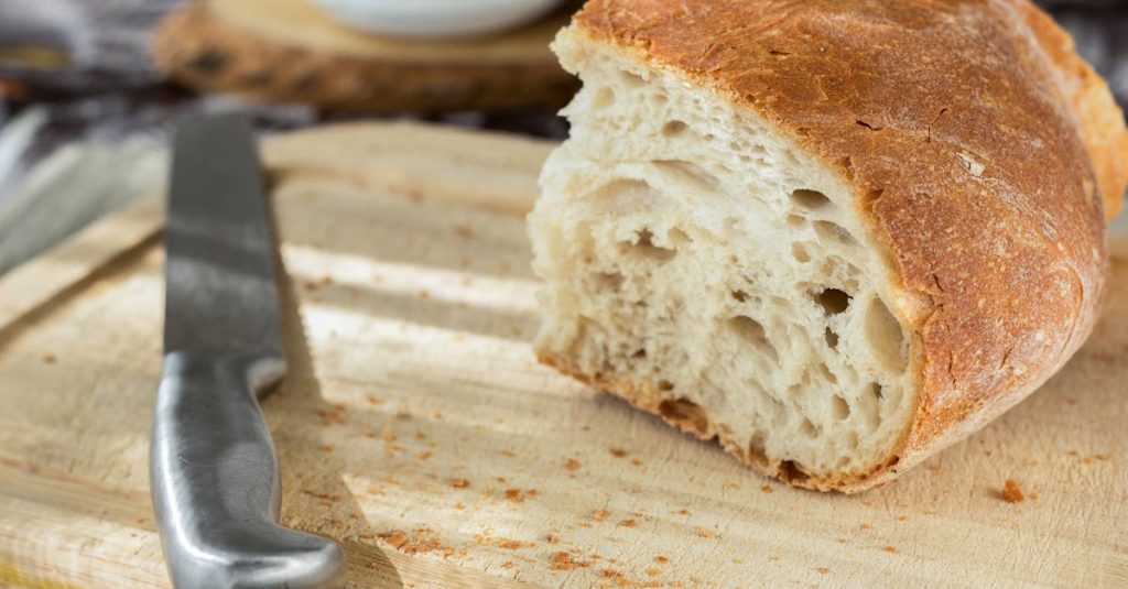 Close-up of a freshly cut loaf of bread on a wooden cutting board with a knife beside it.